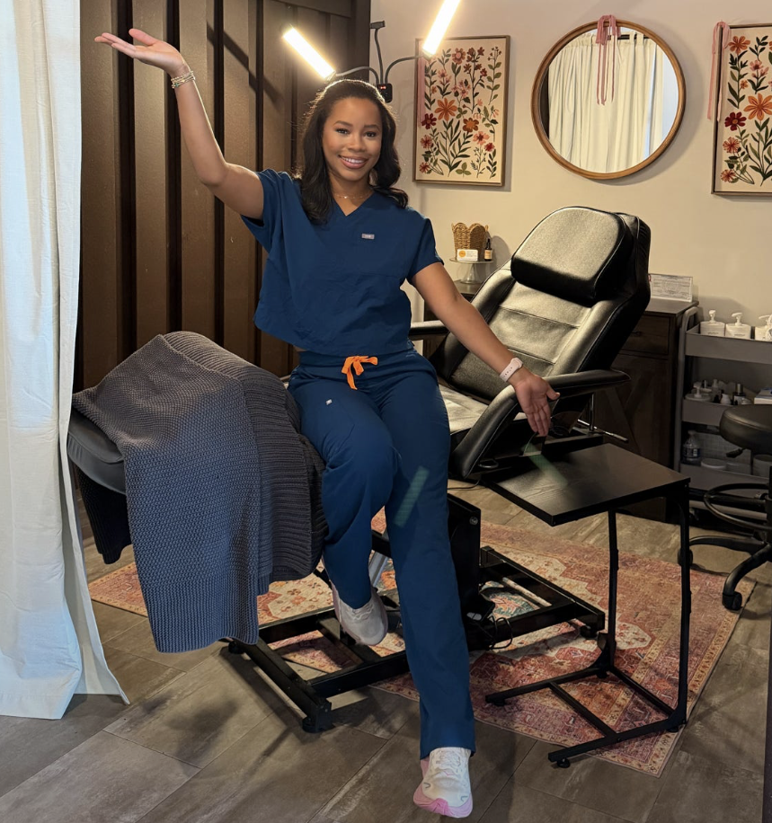 A Shine Auburn esthetician in navy scrubs waving in a treatment room